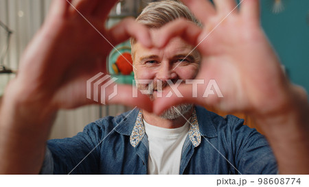Happy middle-aged man makes symbol of love showing heart sign to camera express romantic feelings Happy middle-aged man makes symbol of love showing heart sign to camera express romantic feelings 98608774