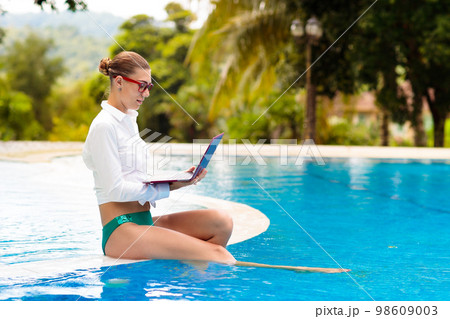 Woman with laptop at swimming pool. Remote work. 98609003