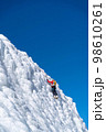A climber in a red suit climbs an icy white mountain 98610261