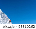 A climber in a red suit climbs an icy white mountain 98610262