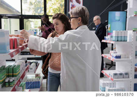 Elderly drugstore worker helping woman customer with spf medical leaflet discussing products prescription. Pharmacist offering support assistance while working in pharmacy. Medicine concept Elderly drugstore worker helping woman customer with spf medical leaflet discussing products prescription. Pharmacist offering support assistance while working in pharmacy. Medicine concept 98610370