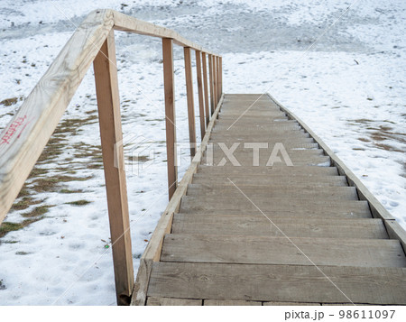 Wooden ladder in the snow. Descent to the water. 98611097