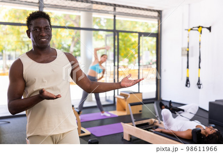 Portrait of African American male fitness instructor inviting to pilates reformer studio Portrait of African American male fitness instructor inviting to pilates reformer studio 98611966