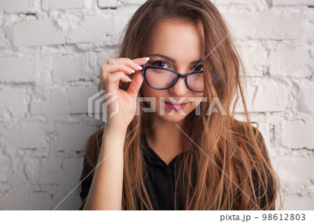 beautiful girl close-up in the glasses smiles against the background of a white wall 98612803