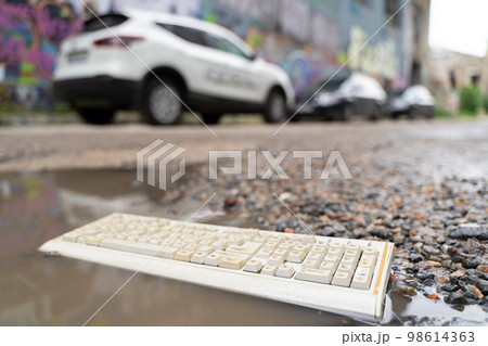 old broken computer keyboard, thrown into the trash lying on the road in a puddle. old broken computer keyboard, thrown into the trash lying on the road in a puddle. 98614363