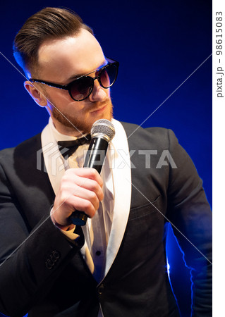 handsome presenter and showman in a stylish suit with a microphone on stage handsome presenter and showman in a stylish suit with a microphone on stage 98615083