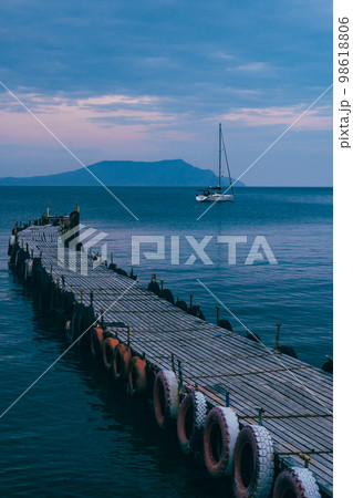 Old wooden fishing pier goes into the sea on sunset. Resort city Novyi Svet, Crimea Old wooden fishing pier goes into the sea on sunset. Resort city Novyi Svet, Crimea 98618806