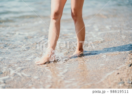 A woman walks along the beach, legs close-up. Barefoot woman sta A woman walks along the beach, legs close-up. Barefoot woman sta 98619511
