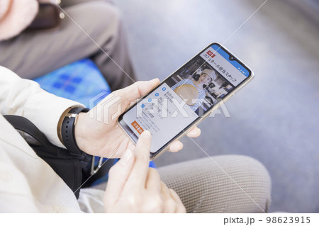 電車内でスマホで求人サイトを見るミドル女性手元 98623915