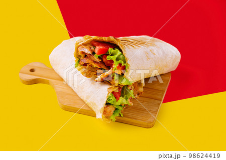 shawarma with chicken, tomatoes and lettuce on a wooden board shawarma with chicken, tomatoes and lettuce on a wooden board 98624419