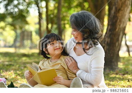 Loving mature grandma embracing and reading fairytale to little grandchild. Family, generation and people concept Loving mature grandma embracing and reading fairytale to little grandchild. Family, generation and people concept 98625601