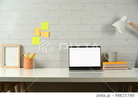 Creative workstation with laptop computer, pencil holder, books and lamp on white table. Empty screen for advertise design Creative workstation with laptop computer, pencil holder, books and lamp on white table. Empty screen for advertise design 98625780