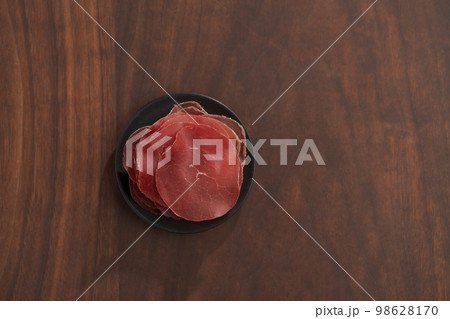 saucer with this slices of bresaola on walnut wood table 98628170