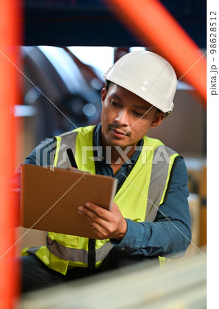 Storehouse worker checking stock and inventory on clipboard while sitting in retail warehouse. Business factory industry concept Storehouse worker checking stock and inventory on clipboard while sitting in retail warehouse. Business factory industry concept 98628512
