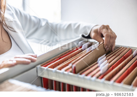 The clerk is leafing through stored folders, looking for a file or document. Concept of data storage, filing cabinet and business administration. 98632583