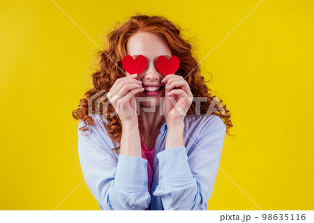pregnant redhead ginger curly woman holding paper heards in studio yellow walls.Valentine's Day pregnant redhead ginger curly woman holding paper heards in studio yellow walls.Valentine's Day 98635116