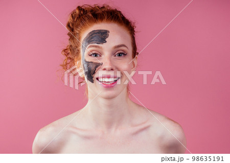 redhaired ginger teenager girl with black clay mask on her pretty face on pink studio background redhaired ginger teenager girl with black clay mask on her pretty face on pink studio background 98635191