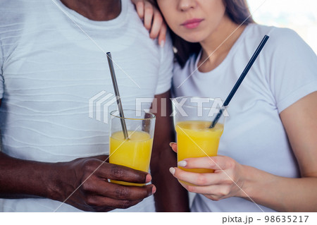 international couple in love holding in hands glasses with orange juice.afro man use disposable tableware,but european woman useing eco steel tubes 98635217