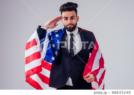 arabian young handsome black hair man in stylish business suit holding american flag in studio isolate white background.Independence Day concept arabian young handsome black hair man in stylish business suit holding american flag in studio isolate white background.Independence Day concept 98635249