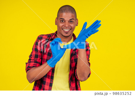 latin brazilian cleaning man wearing ribon gloves in studio yellow background latin brazilian cleaning man wearing ribon gloves in studio yellow background 98635252