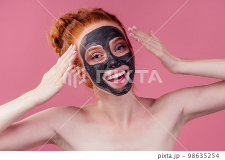 redhaired ginger teenager girl with black clay mask on her pretty face on pink studio background redhaired ginger teenager girl with black clay mask on her pretty face on pink studio background 98635254