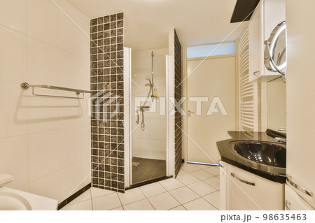 a bathroom with black and white tiles on the walls, shower stall and toilet in the photo is taken to the other side 98635463
