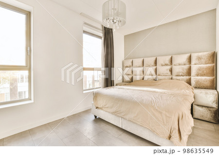 a bedroom with white walls and beige bedding in the middle of the room, there is a chandel on the headboard a bedroom with white walls and beige bedding in the middle of the room, there is a chandel on the headboard 98635549