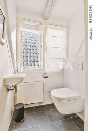 a bathroom with a toilet, sink and window in the corner next to it is a black trash can on the floor a bathroom with a toilet, sink and window in the corner next to it is a black trash can on the floor 98635640