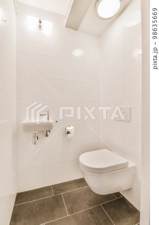 a bathroom with white walls and tile flooring, including a toilet in the center of the photo is a wall mounted mirror 98635669