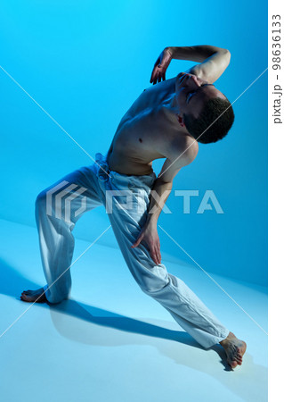 Contemporary dance style. Young artistic man dancing contemp, experimental dance over blue studio background. Flexible artist 98636133