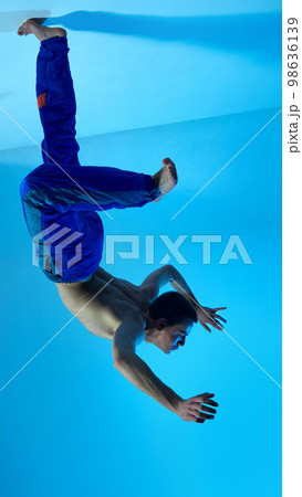 Contemporary dance style. Upside down. Young artistic man dancing contemp, experimental dance over blue studio background. Expressive Contemporary dance style. Upside down. Young artistic man dancing contemp, experimental dance over blue studio background. Expressive 98636139