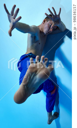 Contemporary dance style. Young artistic man dancing contemp, experimental dance over blue studio background. Impressive performance 98636157