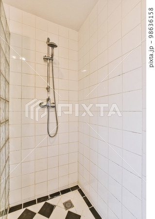 a bathroom with black and white tiles on the floor, shower head is in the center of the tileed wall 98636158