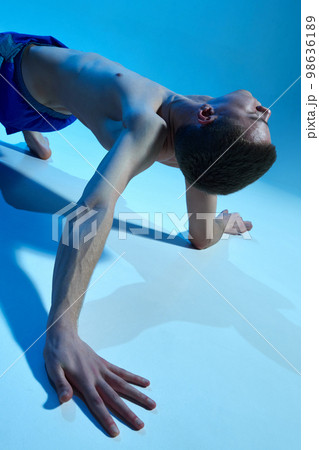 Contemporary dance style. Young shirtless man dancing contemp, experimental dance over blue studio background. Flexible movements Contemporary dance style. Young shirtless man dancing contemp, experimental dance over blue studio background. Flexible movements 98636189