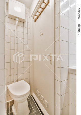 a white toilet in a small bathroom with tile flooring and wall tiles on the walls there is a mirror above it a white toilet in a small bathroom with tile flooring and wall tiles on the walls there is a mirror above it 98636311