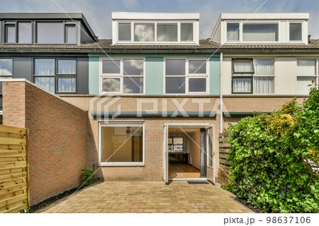 an outside view of a two story town house with brick walls and green plants in the front yard is surrounded by trees an outside view of a two story town house with brick walls and green plants in the front yard is surrounded by trees 98637106