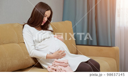 Woman explores baby clothes and awaits future childbirth 98637145
