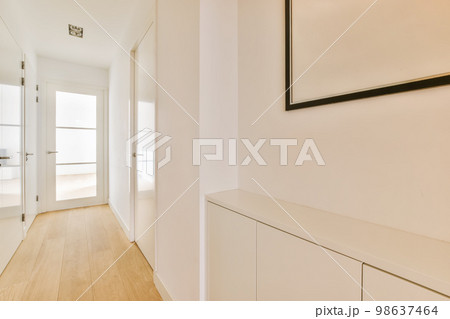 an empty hallway with white walls and wood flooring on either side by the door is a black framed mirror 98637464