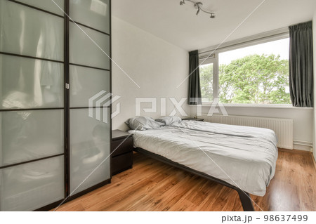 a bedroom with wood flooring and sliding glass doors on the wall to the right is a large bed in front 98637499