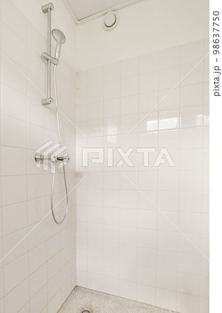 a bathroom with white tiles on the walls and floor, including a shower head mounted in the corner of the bathtub 98637750