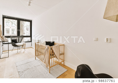 Interior of white room with baby crib and armchair near window with blue chest of drawers in daylight Interior of white room with baby crib and armchair near window with blue chest of drawers in daylight 98637761