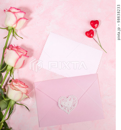 Festive flat lay arrangement of pale pink roses, envelope, hearts, empty white blank sheet on pink. Festive flat lay arrangement of pale pink roses, envelope, hearts, empty white blank sheet on pink. 98638233