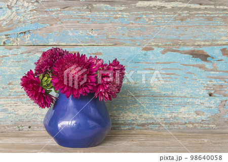 Bouquet of purple asters flowers in blue vase on old blue paint wooden background; copy space 98640058