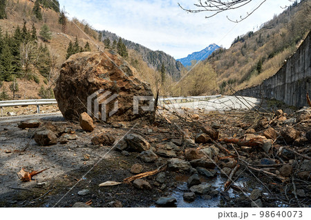 A huge rock fell from the mountains onto the road, destroying the asphalt and blocking half of the roadway 98640073