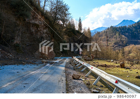 A huge rock fell from the mountains onto the road, destroying the asphalt and blocking half of the roadway 98640097