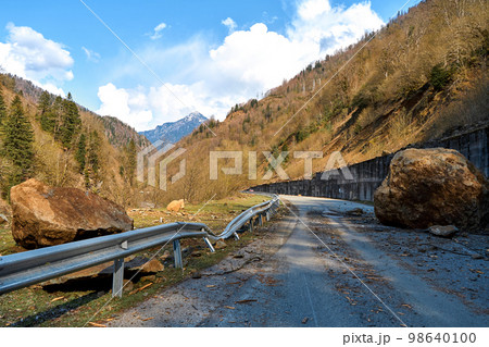 A huge rock fell from the mountains onto the road, destroying the asphalt and blocking half of the roadway 98640100