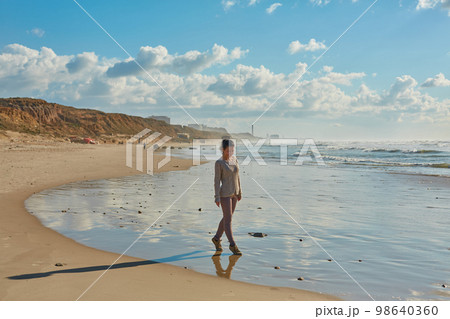 The girl walks along the sea coast. The water is still cold, so she just enjoys the walk 98640360