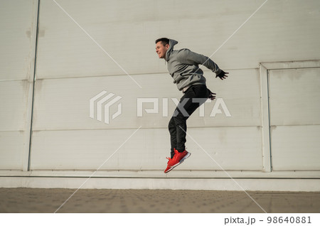 Caucasian man in hoodie jumping high with hands on knees outdoors. Caucasian man in hoodie jumping high with hands on knees outdoors. 98640881