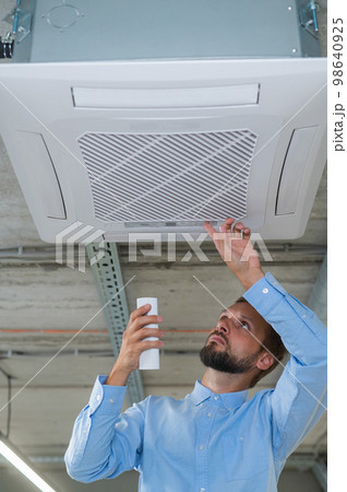 Caucasian bearded man repairing the air conditioner in the office. Caucasian bearded man repairing the air conditioner in the office. 98640925