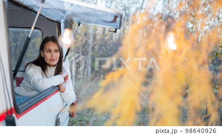 Portrait of a caucasian woman looking out of a trailer window. Travel in a camper in autumn. Portrait of a caucasian woman looking out of a trailer window. Travel in a camper in autumn. 98640926